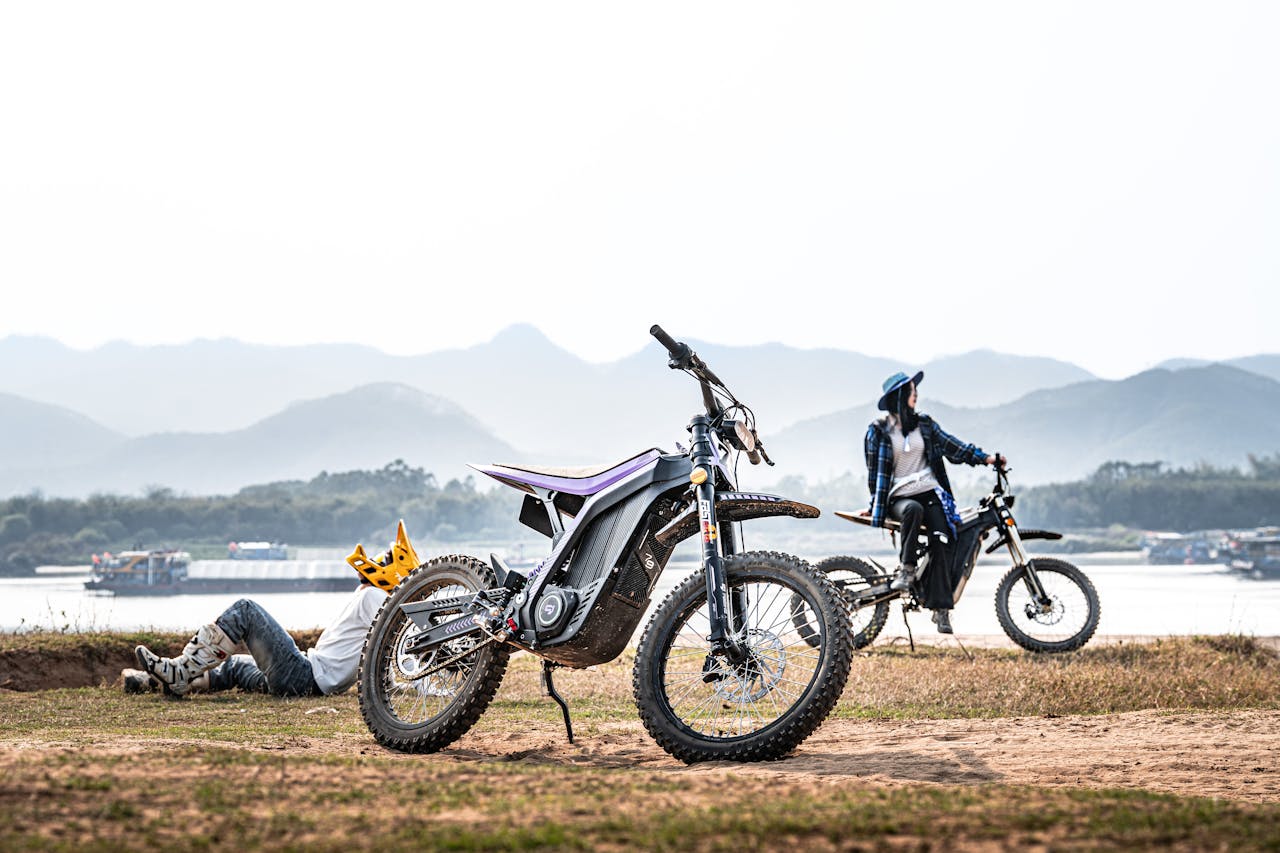 Two individuals on electric dirt bikes near a serene lake with mountains in the background.